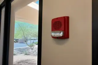 Horn-strobe fire alarm device mounted on an interior wall with desert landscape visible through a window in Phoenix, AZ.