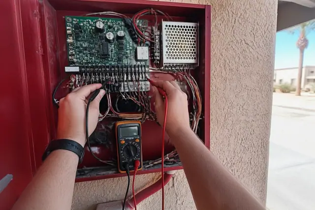 Technician troubleshooting a fire alarm control panel with a multimeter on a jobsite in Phoenix, AZ.