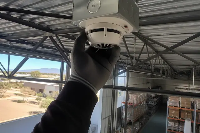 Technician performing maintenance on a high-ceiling heat detector at a warehouse in Phoenix, AZ.