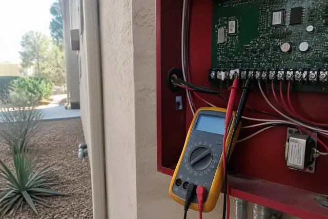 Technician using a multimeter to test a fire alarm terminal block at a building in Phoenix, AZ.