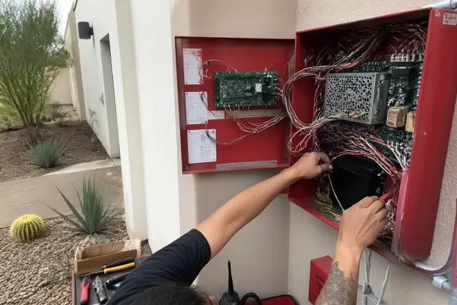 Technician wiring a fire alarm control panel inside a stucco building in Phoenix, AZ.