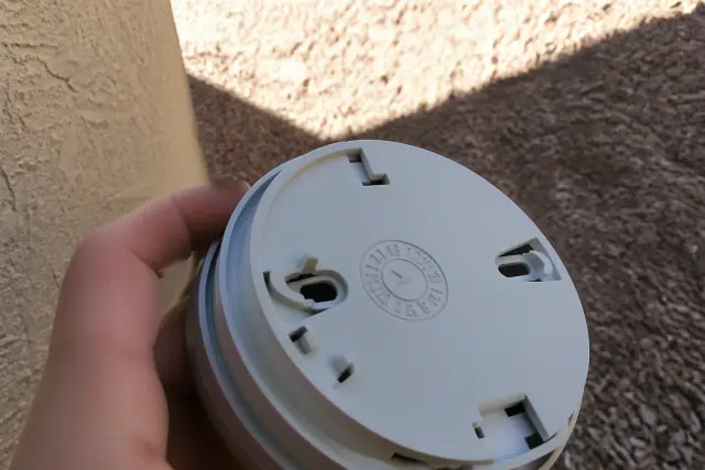 A contractor holding a smoke detector to show the embossed date wheel against a stucco wall in Phoenix, AZ.