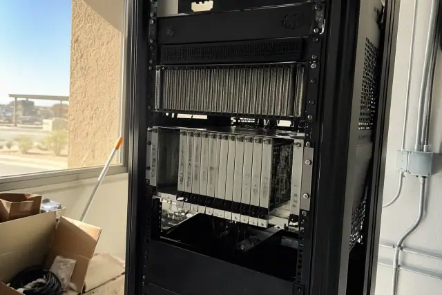 Technician inspecting modular amplifier cards in a voice evacuation server rack at a jobsite in Phoenix, AZ.
