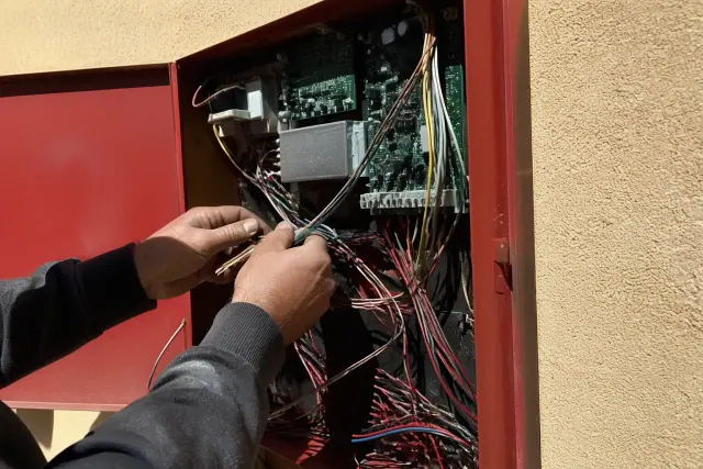 Technician wiring a fire alarm control panel on a stucco wall at a job site in Phoenix, AZ.