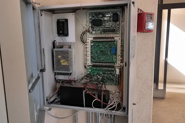 Technician hands wiring a fire alarm control panel inside a building in Phoenix, AZ.