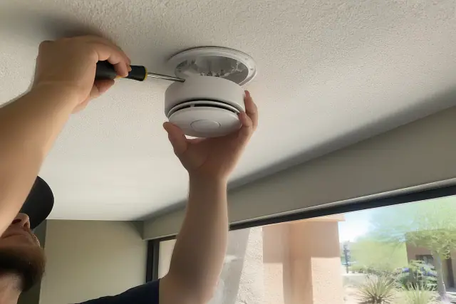 Technician installing a smoke detector on a commercial ceiling in Phoenix, AZ.