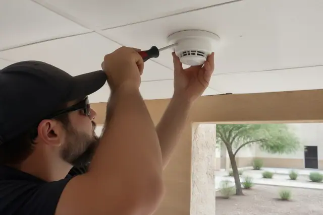 Technician installing a smoke detector on a ceiling junction box at a jobsite in Phoenix, AZ.