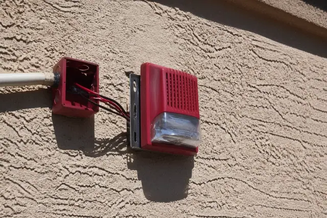 Wall-mounted fire alarm horn-strobe device installed on a stucco exterior wall in Phoenix, AZ.