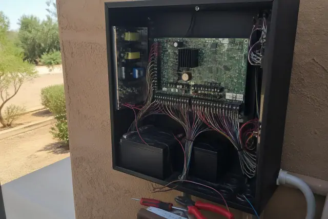 Technician wiring a fire alarm control panel during a retrofit in Phoenix, AZ, with desert landscaping in the background.