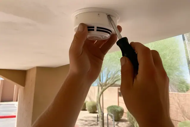 Technician installing a smoke detector on a commercial ceiling in Phoenix, AZ.