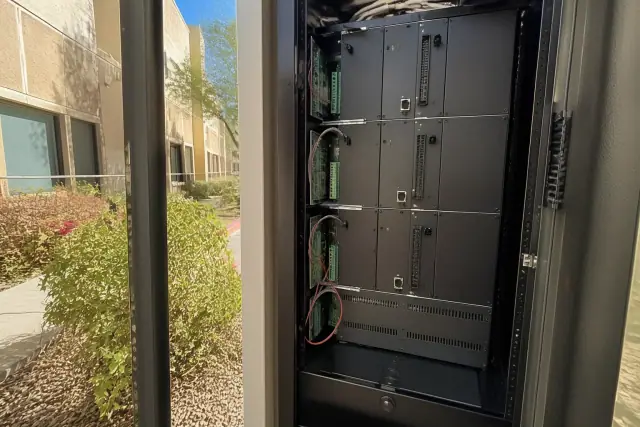 Technician inspecting voice evacuation amplifier cards in a server rack at a Phoenix, AZ commercial building jobsite.