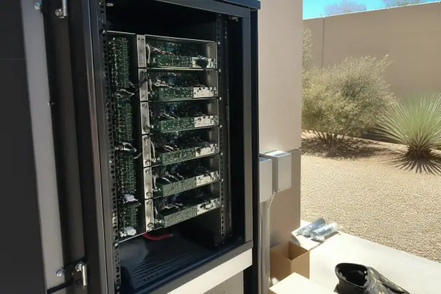 Technician inspecting modular amplifier cards in a fire alarm server rack at a site in Goodyear, AZ.