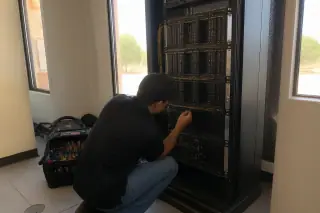 Technician inspecting wiring in a voice evacuation amplifier rack at a Phoenix, AZ jobsite.