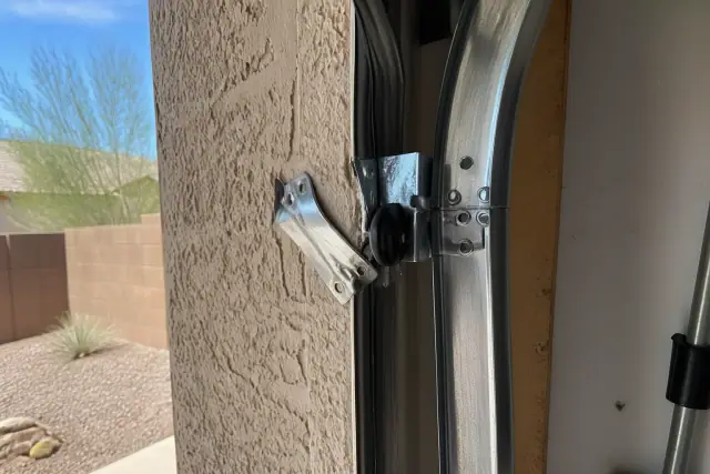 Bent garage door track bracket with structural damage on a stucco wall in Phoenix, AZ.
