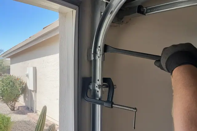 Technician using a pry bar and C-clamp to straighten a bent garage door track at a home in Phoenix, AZ.