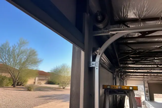 Commercial garage door repair showing a high-lift track system and steel cable at a job site in Surprise, AZ.