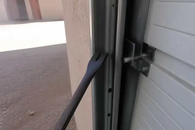 Technician using a pry bar to realign an off-track commercial garage door in Phoenix, AZ.