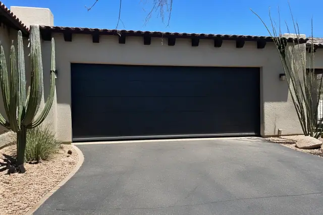 A newly installed garage door on a stucco home with desert landscaping and a gravel driveway in Phoenix, AZ.