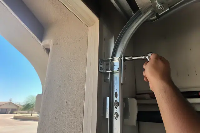 Technician using a socket wrench to install a new heavy-duty steel garage door track at a home in Phoenix, AZ.