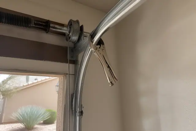 Locking pliers clamped to a garage door track for cable replacement in a Phoenix, AZ home garage.