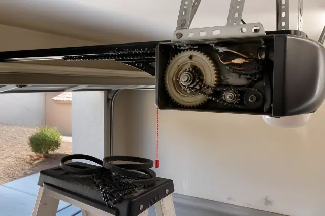 Open garage door opener motor showing internal gears, chain, and belt fragments on a ladder in Phoenix, AZ.