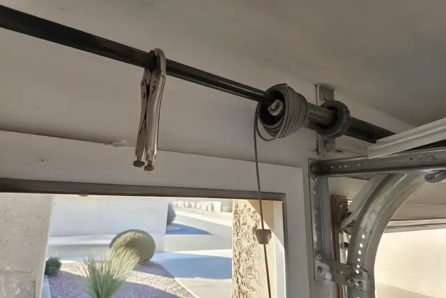 Garage door cable repair showing pulleys, a lifting cable, and a torsion bar in a Glendale, AZ garage workspace.