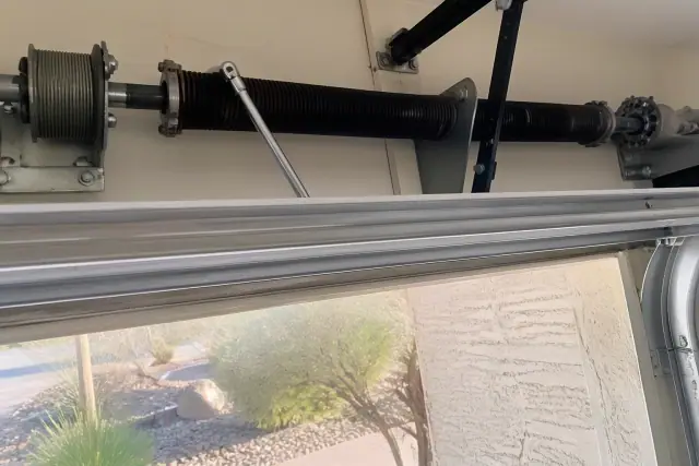 Torsion spring garage door maintenance with tools and lubricant on a metal shaft at a home in Surprise, AZ.