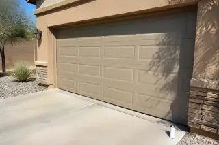 Fully operational garage door with desert landscaping and a lubricant can on a driveway in Phoenix, AZ.