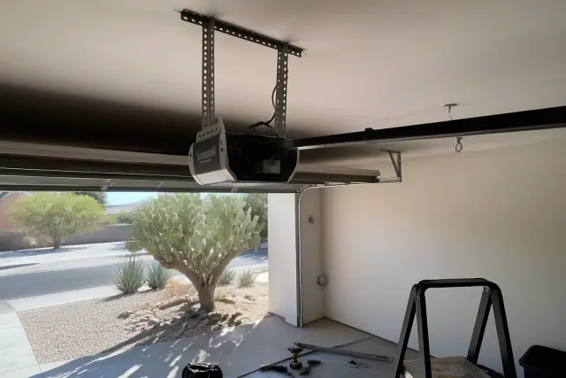 Garage door opener motor being installed on ceiling brackets in a garage in Tempe, AZ with desert plants outside.