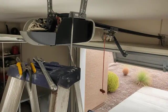 Technician performing garage door opener repair with tools on a ladder in Chandler, AZ.