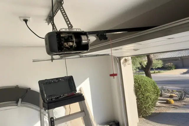 Technician repairing a garage door opener motor on a ceiling mount in Tempe, AZ.
