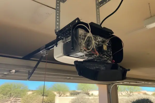 Technician repairing a garage door opener motor with exposed wiring in Goodyear, AZ.