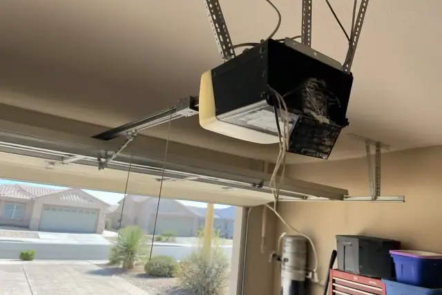 Garage door opener motor with a loose wiring harness and detached panel in an Avondale, AZ residential garage.