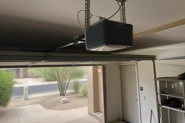 Garage door opener motor mounted to a ceiling in a Phoenix, AZ garage with desert landscaping visible outside.