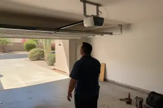 Technician inspecting a garage door opener motor mounted to the ceiling in a Phoenix, AZ home.