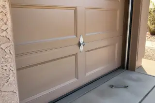 New garage door panel and mounting hinge on a stucco home in Phoenix, AZ with a wrench on the concrete floor.