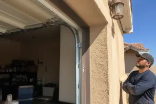 Technician observing new garage door rollers in metal tracks on a stucco home in Phoenix, AZ.