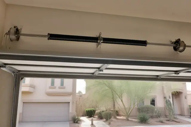 Torsion spring installation on a garage door shaft in Phoenix, AZ, with desert landscaping in the background.