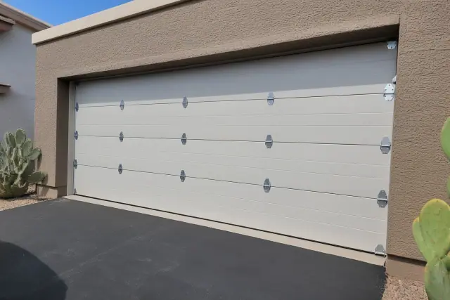 New garage door with metal hinges and brackets on a home in Goodyear, AZ with an asphalt driveway and desert landscaping.