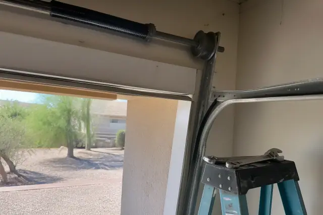 Misaligned garage door track and rollers in a Phoenix, AZ garage with tools on a ladder.