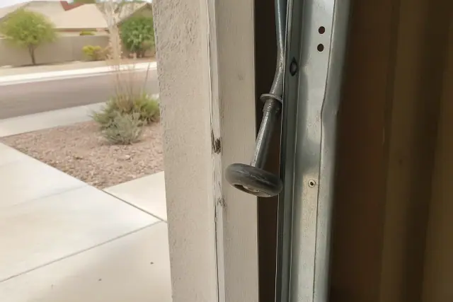 A detached garage door roller hanging from a bent metal track on a stucco home in Gilbert, AZ.