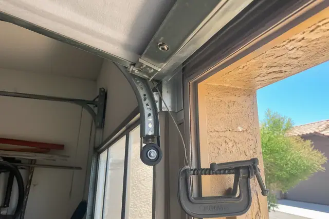 A garage door roller dangling from its track with a loose cable during a repair job in Chandler, AZ.