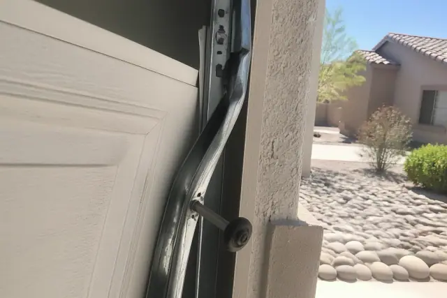 Garage door repair showing a misaligned panel and detached roller on a twisted track at a home in Goodyear, AZ.
