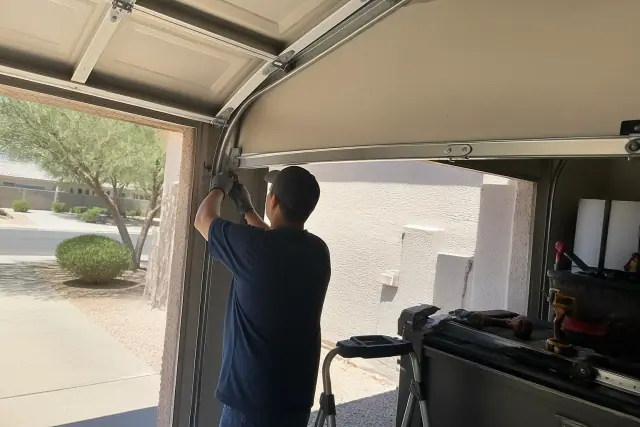 A technician repairing garage door tracks, panels, and rollers at a home in Phoenix, AZ.