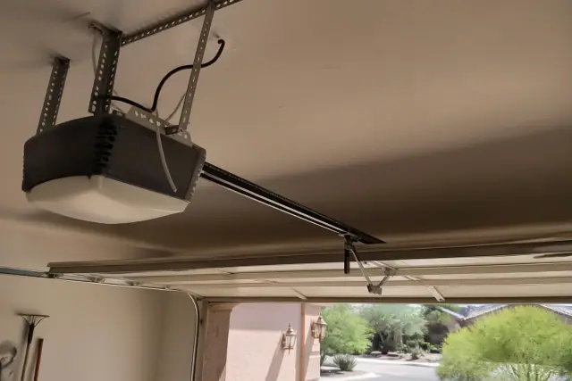 Garage door opener motor and rail mounted to a ceiling in Phoenix, AZ, with desert landscaping visible in the background.