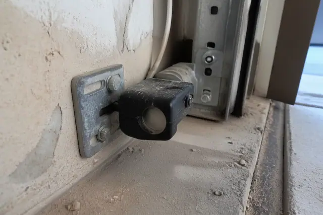 Dust-covered garage door safety sensor near floor tracks in a Phoenix, AZ garage.