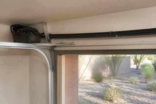 Technician's view of garage door track and spring maintenance in Phoenix, AZ with tools resting on the header.