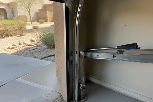 Garage door track repair in progress on a stucco home in Phoenix, AZ, showing rollers and brackets on the metal tracks.