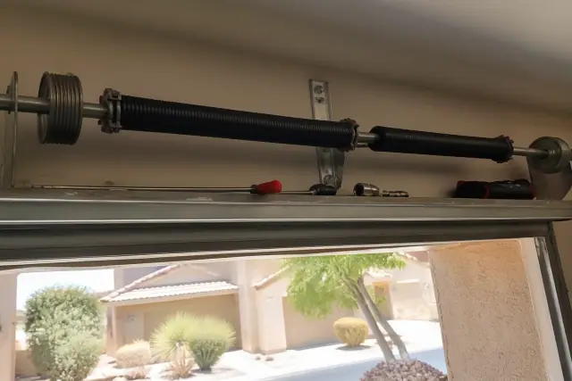 Technician repairing residential garage door torsion springs on a metal shaft at a home in Phoenix, AZ.
