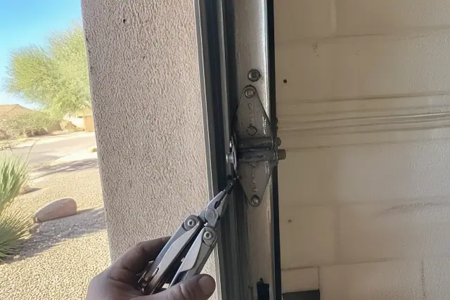 Technician inspecting garage door hinges, rollers, and brackets on a stucco wall in Phoenix, AZ.